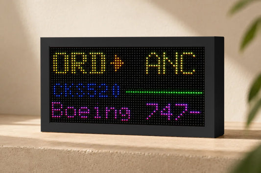 Mach 2 Lite LED flight tracker in a matte black case on a stone shelf, showing a flight from ORD to ANC